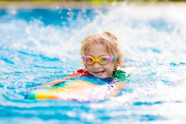 Çocuk tropikal tatil köyü havuzunda yüzmeyi öğreniyor. Çocuklar yüzmeyi öğrenir. Küçük çocuklar için egzersiz ve eğitim. Spor kulübünde renkli sörf tahtası olan küçük bir çocuk. Yüzen bebek ya da bebek.