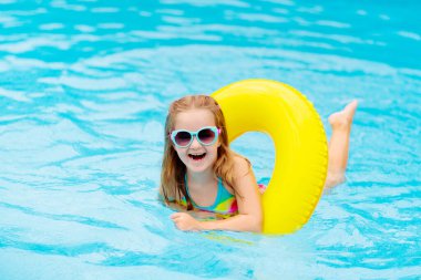Yüzme havuzunda yüzen bir çocuk. Çocuklar yüzer. Küçük çocuklar için renkli sarı yüzer. Küçük kız yaz tatilinde tropikal tatil köyünde eğleniyor. Plaj ve su oyuncakları. Güneş koruması.