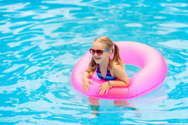 Yüzme havuzunda yüzen bir çocuk. Çocuklar yüzer. Genç çocuklar için renkli gökkuşağı yüzüyor. Küçük kız yaz tatilinde tropikal tatil köyünde eğleniyor. Plaj ve su oyuncakları. Güneş koruması.