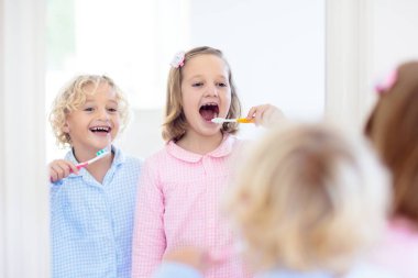 Dişlerini fırçalayan çocuk. Diş macunu ve fırçası olan çocuklar. Diş ve ağız temizliği, bakım. Çocuklar için sağlıklı günlük rutin. Çocuk duştan sonra veya evde banyo yaptıktan sonra. Diş macunlu pijamalı kız ve oğlan..