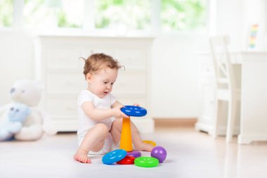 Bebek renkli oyuncaklar ile oynuyor. Genç çocuk için eğitim oyuncak yığını. Çocuklar evde oynar. Piramit ve top ile beyaz güneşli kreş küçük kız.