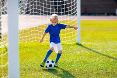 Çocuklar stadyum sahasında futbol oynarlar. Çocuklar futbol maçında gol atıyor. Küçük çocuk topa vuruyor. Okul spor kulübü. Genç oyuncu için alıştırma.