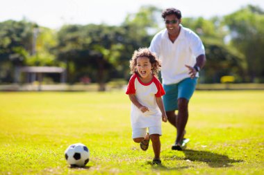 Baba ve oğlu futbol oynuyor. Baba ve küçük çocuk futbol oynuyorlar. Genç aktif aile açık havada güneşli bir yaz gününün tadını çıkarıyor. Çocuklar için sağlıklı bir spor. Futbol kulübü..