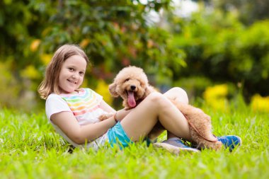 Kids sevimli küçük köpek yavrusu ile oynamak. Çocuk ve bebek köpekler güneşli yaz bahçede oynarken. Küçük kız holding yavru. Çocuk ile evde beslenen hayvan köpek. Aile ve park'ın bahçesinde evcil hayvan. Çocuk ve hayvan dostluk.