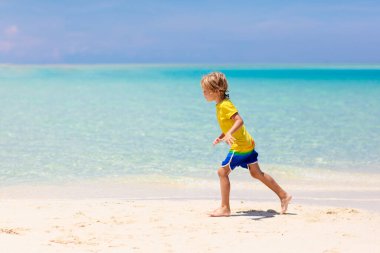Tropik plajda oynayan çocuklar. Çocuklar yaz tatilinde yüzer ve denizde oynarlar. Kum ve su eğlencesi, küçük çocuklar için güneş koruması. Küçük çocuk ve kız okyanus kıyısında koşup zıplıyorlar..