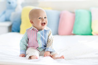 Beyaz yatak odasındaki bebek. Pastel renkli yastıkla yatakta yeni doğmuş bir çocuk. Çocuklar için çocuk odası. Tekstil, yastık ve çocuklar için yatak. Aile sabahı evde. Oyuncak ayıyla karnını doyuran yeni doğmuş çocuk..
