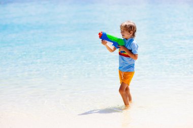 Çocuk oyuncak su tabancasıyla oynuyor. Tatil ve plaj eğlencesi. Çocuklar tropik ada beldesinde plastik tabancayla koşup oynuyorlar. Aile yaz tatili aktiviteleri denizde. Çocuklarla seyahat et.. 