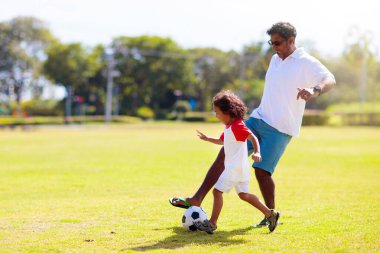 Baba ve oğlu futbol oynuyor. Baba ve küçük çocuk futbol oynuyorlar. Genç aktif aile açık havada güneşli bir yaz gününün tadını çıkarıyor. Çocuklar için sağlıklı bir spor. Futbol kulübü..