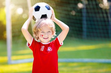 Danimarka futbolu taraftarı tezahürat yapıyor. Danimarkalı çocuklar futbol oynar ve dışarıda zaferi kutlarlar. Danimarka takımı destekçisi. Dansk bayraklı formalı küçük çocuk topa vuruyor. Çocuklar için spor eğitimi.