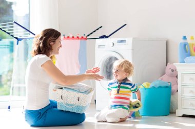 Anne ve çocuklar Çamaşırhane, çamaşır makinesi ile Oda veya kurutma. Aile işleri. Modern ev aygıtları ve çamaşır deterjan beyaz güneşli evinde. Raf kurutma üzerinde temiz yıkanmış kıyafetler. 