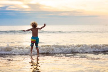 Okyanus plaj üzerinde oynayan çocuk. Dalgalar halinde günbatımında atlama çocuk. Deniz tatil aile ile çocuklar için. Egzotik ada tropik sahilde yaz tatili sırasında çalışan çocuk. Çocuklar için giyim yüzmek