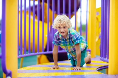 Çocuk dışarıda oyun oynuyordu. Çocuklar okulda ya da anaokulunda oynarlar. Aktif çocuk renkli kayıyor ve sallanıyor. Çocuklar için sağlıklı bir yaz aktivitesi. Küçük çocuk dışarı tırmanıyor..