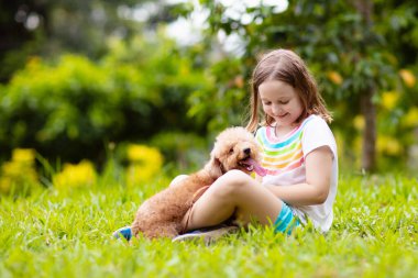 Kids sevimli küçük köpek yavrusu ile oynamak. Çocuk ve bebek köpekler güneşli yaz bahçede oynarken. Küçük kız holding yavru. Çocuk ile evde beslenen hayvan köpek. Aile ve park'ın bahçesinde evcil hayvan. Çocuk ve hayvan dostluk.