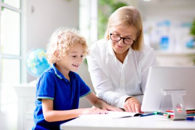 Çevrimiçi uzaktan öğrenme. Bilgisayarlı okul çocukları öğretmen ve sınıf grubuyla görüntülü konuşma yapıyorlar. Anne oğluna yardım ediyor. Çocuk evden ders çalışıyor. Koronavirüs salgınında evde eğitim.