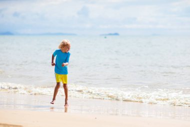 Tropik plajda oynayan çocuklar. Çocuklar yaz tatilinde yüzer ve denizde oynarlar. Kum ve su eğlencesi, küçük çocuklar için güneş koruması. Okyanus kıyısında koşan ve zıplayan küçük çocuk.