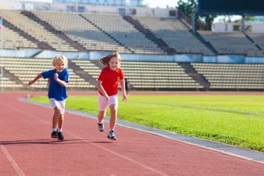 Stadyumda çalışan çocuk. Çocuklar açık pistte çalışır. Çocuklar için sağlıklı spor aktivitesi. Atletizm yarışında küçük kız ve çocuk. Genç atlet eğitimi. Runner egzersiz. Çocuk için jogging.
