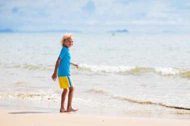 Tropik plajda oynayan çocuklar. Çocuklar yaz tatilinde yüzer ve denizde oynarlar. Kum ve su eğlencesi, küçük çocuklar için güneş koruması. Okyanus kıyısında koşan ve zıplayan küçük çocuk.