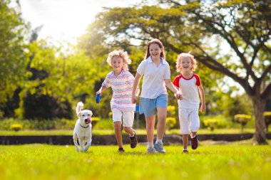 Güneşli yaz gününde dışarıda koşan çocuklu bir aile. Kardeşler bahçede oynarlar. Çocuk ve kız parkta köpek gezdiriyorlar. Çocuk ve evcil hayvanla tatil. Bir grup okul çocuğu bir köpek yavrusuyla koşuyor..