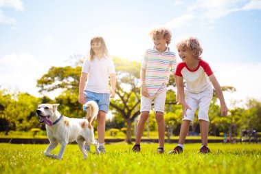 Güneşli yaz gününde dışarıda koşan çocuklu bir aile. Kardeşler bahçede oynarlar. Çocuk ve kız parkta köpek gezdiriyorlar. Çocuk ve evcil hayvanla tatil. Bir grup okul çocuğu bir köpek yavrusuyla koşuyor..