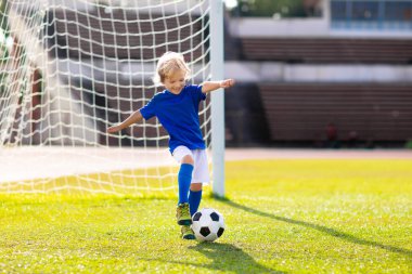 Çocuklar stadyum sahasında futbol oynarlar. Çocuklar futbol maçında gol atıyor. Küçük çocuk topa vuruyor. Okul spor kulübü. Genç oyuncu için alıştırma.