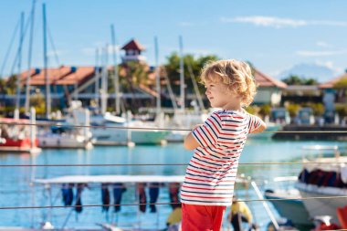 Child watching yacht and boat in harbor. Yachting sport for family with kids. Little boy walking in tropical resort on summer vacation. Nautical fashion for children. Holiday at the sea.
