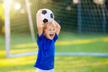 Çocuklar stadyum sahasında futbol oynarlar. Çocuklar futbol maçında gol atıyor. Küçük çocuk topa vuruyor. Okul spor kulübü. Genç oyuncu için alıştırma.
