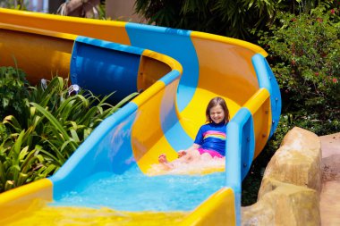 Su parkında su kayağı yapan çocuklar. Çocuklar yaz tatilinde tropik tatil köylerinde su kaydırağında eğleniyorlar. Islak çocuk ve bebek parkı olan eğlence parkı.