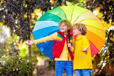 Sonbahar yağmurunda oynayan çocuk. Şemsiyeli çocuk. Sonbahar sezonunda parkta koşan küçük bir çocuk. Her havada çocuklar için açık hava eğlencesi. Çocuklar için su geçirmez giysi, bot ve ceket..