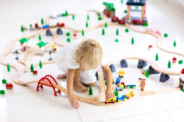 Çocuklar ahşap demiryolu ile oynarlar. Oyuncak trenli çocuk. Küçük çocuklar için eğitici oyuncaklar. Küçük bir çocuk, beyaz zeminde ya da anaokulunda demiryolu inşa ediyor. Araba ve motor çalan sevimli bir çocuk..