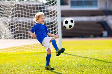 Çocuklar stadyum sahasında futbol oynarlar. Çocuklar futbol maçında gol atıyor. Küçük çocuk topa vuruyor. Okul spor kulübü. Genç oyuncu için alıştırma.