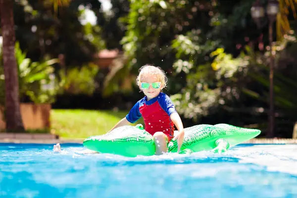 stock image Child playing in swimming pool. Kids learn to swim. Little baby boy with inflatable toy float playing in water on summer vacation in tropical resort. Kid with toy crocodile on beach holiday.