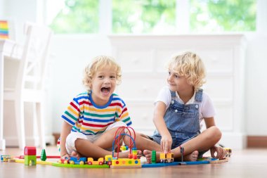 Çocuklar ahşap demiryolu ile oynarlar. Oyuncak trenli çocuk. Küçük çocuklar için eğitici oyuncaklar. Küçük bir çocuk, beyaz zeminde ya da anaokulunda demiryolu inşa ediyor. Araba ve motor çalan sevimli bir çocuk..