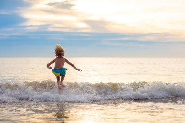 Okyanus plaj üzerinde oynayan çocuk. Dalgalar halinde günbatımında atlama çocuk. Deniz tatil aile ile çocuklar için. Egzotik ada tropik sahilde yaz tatili sırasında çalışan çocuk. Çocuklar için giyim yüzmek