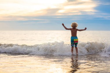 Okyanus plaj üzerinde oynayan çocuk. Dalgalar halinde günbatımında atlama çocuk. Deniz tatil aile ile çocuklar için. Egzotik ada tropik sahilde yaz tatili sırasında çalışan çocuk. Çocuklar için giyim yüzmek