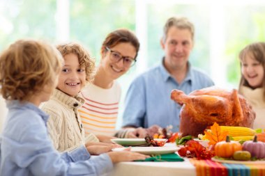 Şükran Günü yemeğinde aile yemeği. Ebeveynler ve çocuklar kızarmış hindi ve sebzeleri severler. Anne, baba ve çocuklar birlikte şenlikli yemek yiyorlar. Sonbahar tatili ev dekorasyonu ve masa düzenleme.