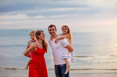 Tropik sahilde çocuklu mutlu bir aile. Deniz tatili. Ebeveynler ve çocuklar gün batımında okyanus kıyısında yürüyorlar. Yaz eğlencesi. Bebek ve küçük çocukla seyahat et. Anne, baba, oğul ve kız oynuyor..