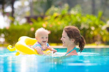 Anne ve bebek tropikal tatil köylerinin havuzunda yüzüyorlar. Çocuk yüzmeyi öğreniyor. Anne ve çocuk suda oynuyorlar. Egzotik bir yerde aile tatili. Çocuklar için aktif ve sağlıklı spor.