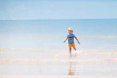 Tropik plajda oynayan çocuklar. Çocuklar yaz tatilinde yüzer ve denizde oynarlar. Kum ve su eğlencesi, küçük çocuklar için güneş koruması. Okyanus kıyısında koşan ve zıplayan küçük çocuk.