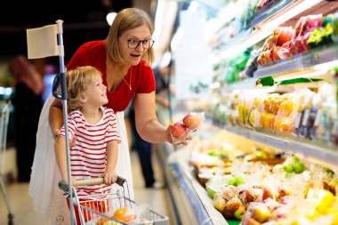 Shopping with kids. Mother and child buying fruit in supermarket. Mom and little boy buy fresh mango in grocery store. Family in shop. Parent and children in a mall choosing vegetables. Healthy food.