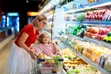 Shopping with kids. Mother and child buying fruit in supermarket. Mom and little boy buy fresh mango in grocery store. Family in shop. Parent and children in a mall choosing vegetables. Healthy food.