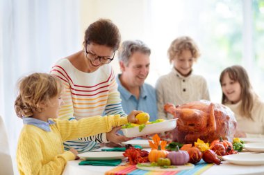 Şükran Günü yemeğinde aile yemeği. Ebeveynler ve çocuklar kızarmış hindi ve sebzeleri severler. Anne, baba ve çocuklar birlikte şenlikli yemek yiyorlar. Sonbahar tatili ev dekorasyonu ve masa düzenleme.