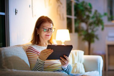 Evde akıllı telefonu olan bir kadın. Kıdemli bayan cep telefonundan mesaj atıyor ya da mesaj kutusunu kontrol ediyor. Hücresi olan bir kadın. Mesaj ve sosyal medya. Modern cihaz. Kız okuyor ve arkadaşlarını arıyor..