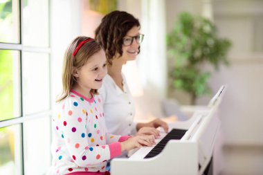 Piyano çalan çocuk. Çocuklar müzik çalar. Çocuklar için klasik eğitim. Sanat dersi. Beyaz dijital klavyede küçük bir kız. Genç öğrenciler için bir araç. Okulda ya da evde müzik dersi.