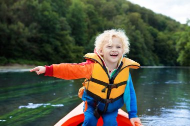 Kano üzerinde kürek çeken çocuk. Çocuklar için yaz kampı. Ailemle kano ve kano gezisi. Kanodaki çocuklar. Küçük çocuk kanoya biniyor. Yaz tatilinde vahşi doğa ve su eğlencesi. Kamp ve balıkçılık.