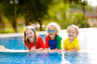 Çocuklar yüzme havuzunda oynar. Çocuklar aile yaz tatili tropikal resort açık yüzme havuzunda yüzmeyi öğrenmek. Su ve splash eğlenmek için tatil genç çocuk. Çocuk ve bebek için güneş koruma.