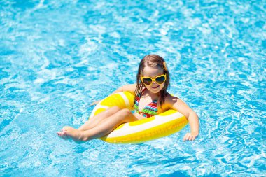 Havuzda yüzen çocuk şişme sarı limon halkası takıyor. Küçük kız turuncu yüzgeçle yüzmeyi öğreniyor. Bebek ve bebek için su oyuncağı. Çocuklar için sağlıklı bir açık hava sporu. Çocuklar plaj eğlencesi.  