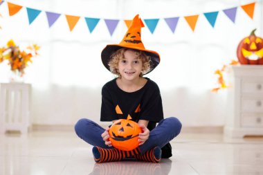 Cadılar Bayramı 'nda cadı kostümü giymiş küçük bir kız ve oğlan. Çocuklar balkabağı kovasında şeker tutuyorlar. Çocuklar Cadılar Bayramı 'nı süslü şöminede kutluyor. Aile şakası mı şeker mi.