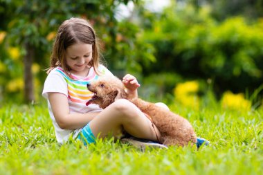 Kids sevimli küçük köpek yavrusu ile oynamak. Çocuk ve bebek köpekler güneşli yaz bahçede oynarken. Küçük kız holding yavru. Çocuk ile evde beslenen hayvan köpek. Aile ve park'ın bahçesinde evcil hayvan. Çocuk ve hayvan dostluk.
