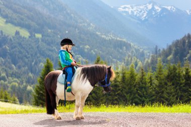 Alp dağlarında midilliye binen çocuklar. Avusturya 'daki at çiftliğinde aile tatili, Tirol. Çocuklar ata biner. Çocuk hayvanla ilgileniyor. Çocuk ve evcil hayvan. Midilli üstünde küçük bir çocuk..