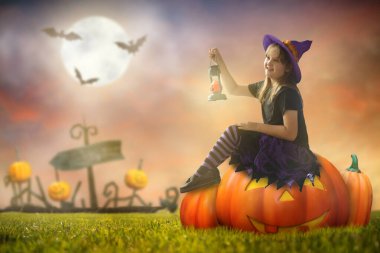 Cadılar Bayramı gecesi dev kabak fenerinin üzerinde oturan küçük cadı. Dolunay ve arka planda yarasalar. Çocuklar şaka mı şeker mi kostümü giyiyor. Çocuklar eğlensin. Ürkütücü ve korkutucu bir kutlama.. 